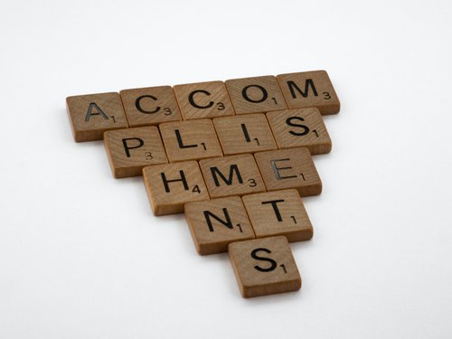 "Accomplishments" spelled out in wooden Scrabble tiles in the shape of a triangle