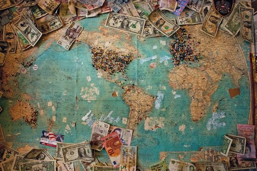 Money from various countries bordering a map of the world, with pins in the map, primarily in the U.S., Europe, and Australia.