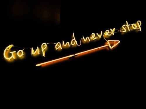 "Go up and never stop" written in neon, with an arrow