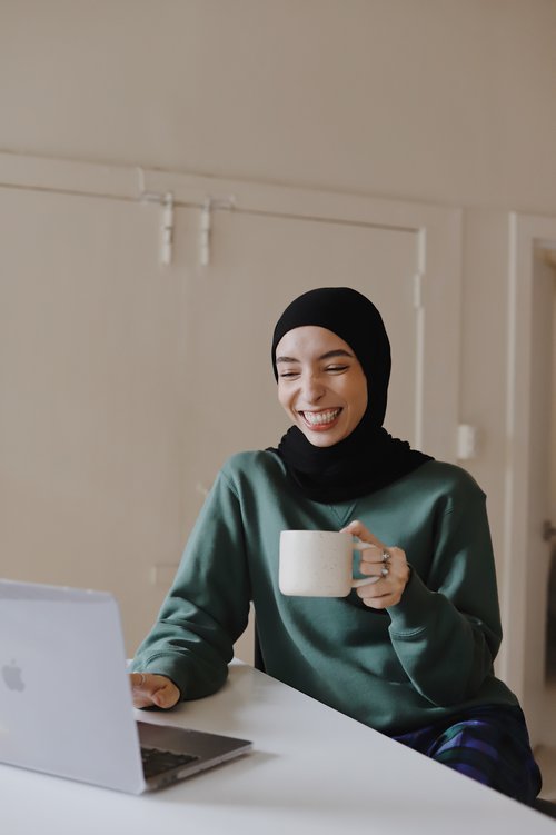 Smiling woman in front of a computer at home holding a mug
