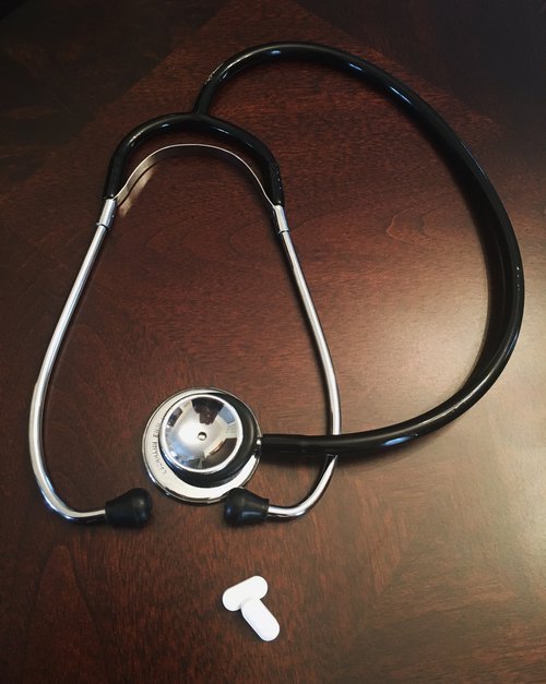 Stethoscope and 2 white pills on a wooden table