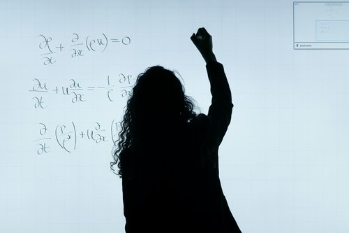 Person in silhouette writing a formula on a white board